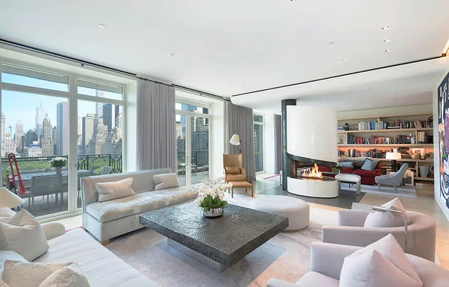 Luxurious living room with modern furniture, large windows, a city view, and a central fireplace.
