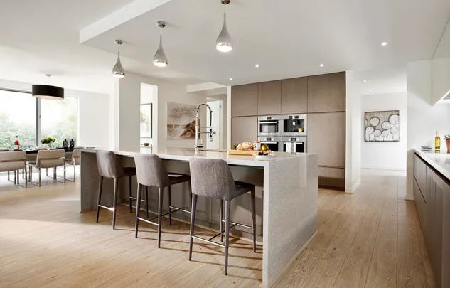 Modern kitchen with island, bar stools, pendant lights, and built-in appliances. Dining area visible in the background.
