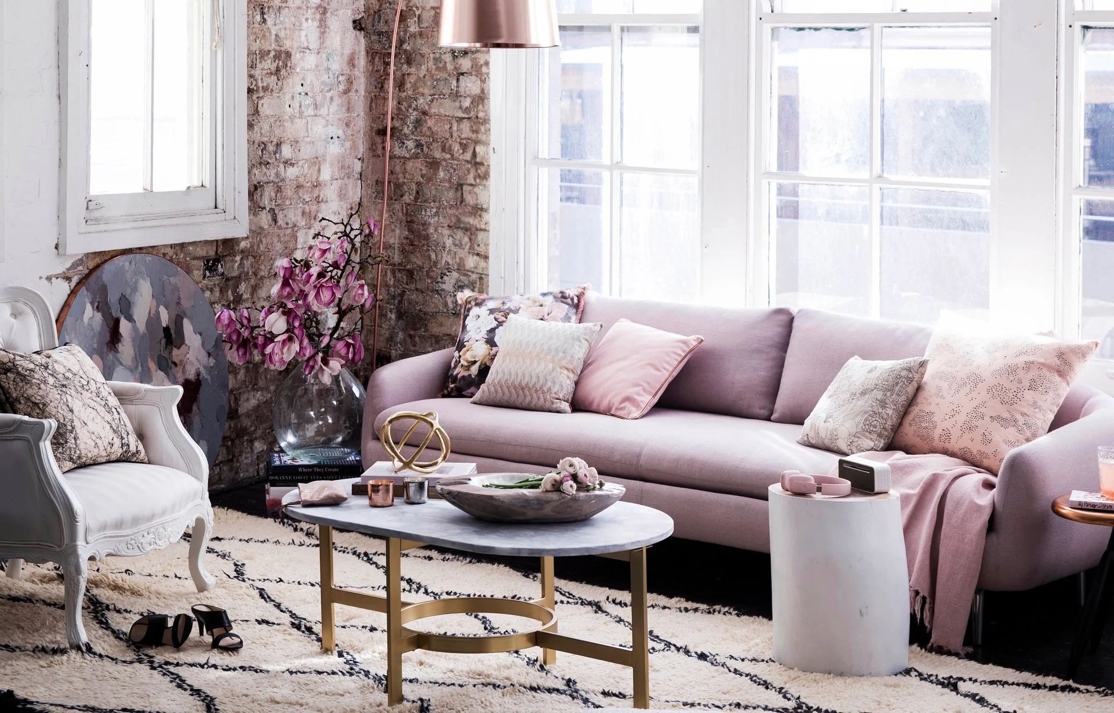Living room with a pink sofa, patterned cushions, metallic coffee table, and brick accent wall with pink flowers.