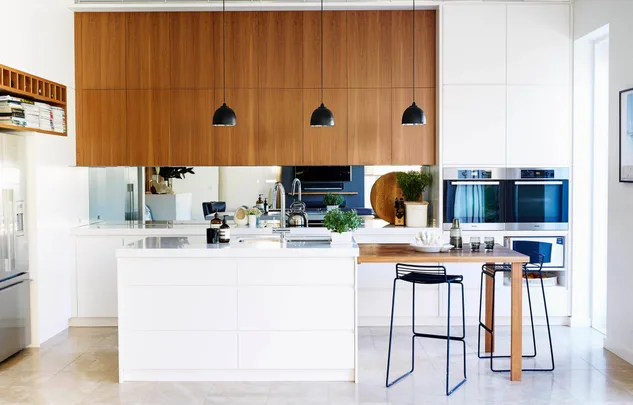 Modern kitchen with white cabinets, wooden accents, black pendant lights, and a central island with plants and decor.