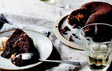Chocolate cake with a slice on a plate, served with cream, and a glass of white wine next to it.