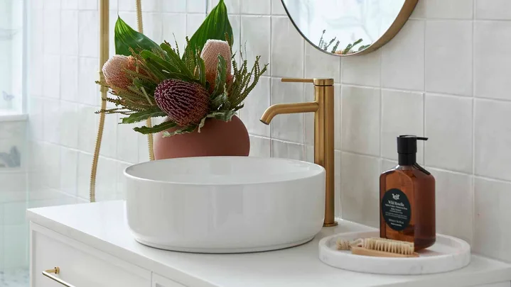 Renovated warm white modern bathroom with white vanity and basin and gold tapware
