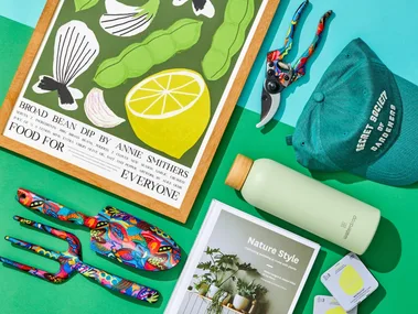 Gifts for gardeners including spades, forks and gardening coffee table books arranged on a blue and green table.