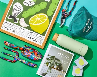 Gifts for gardeners including spades, forks and gardening coffee table books arranged on a blue and green table.