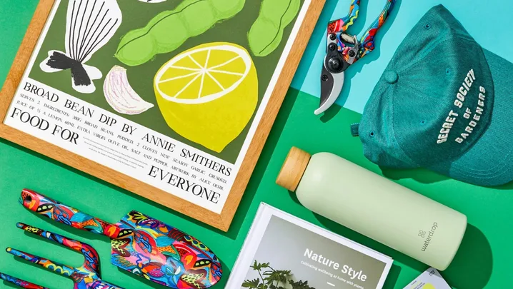 Gifts for gardeners including spades, forks and gardening coffee table books arranged on a blue and green table.