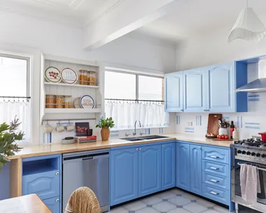 A bright kitchen with blue cabinets, stainless steel appliances, a wooden countertop, and decorative plates on shelves.
