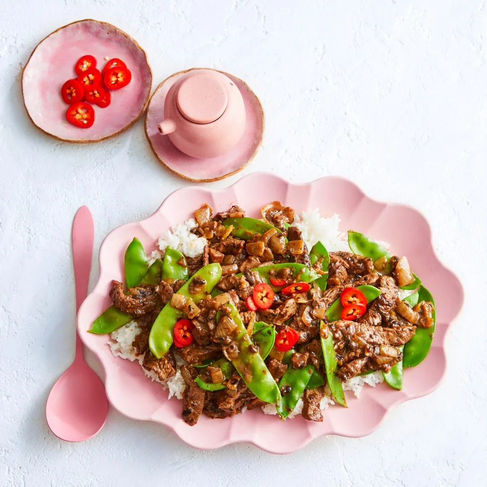 beef and black bean stir fry with snap peas and chili on top in scalloped pink bowl