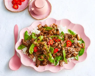 beef and black bean stir fry with snap peas and chili on top in scalloped pink bowl