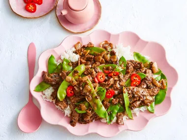 beef and black bean stir fry with snap peas and chili on top in scalloped pink bowl