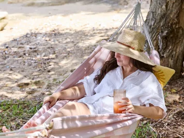 a woman wearing hat and white shirt lounging in a pink hammock