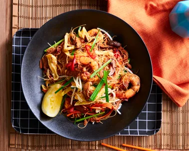 singapore noodles in black bowl with slice of lemon the side