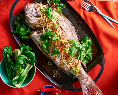 whole snapper fish with fresh herbs on top on black plate
