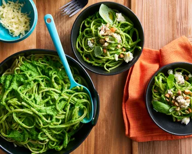 bright green pasta sauce with spaghetti in it in black bowls