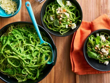 bright green pasta sauce with spaghetti in it in black bowls