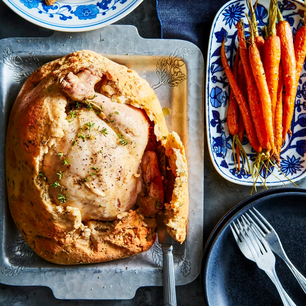 chicken in a salt crust with hole cut out of top with roasted carrots on the side