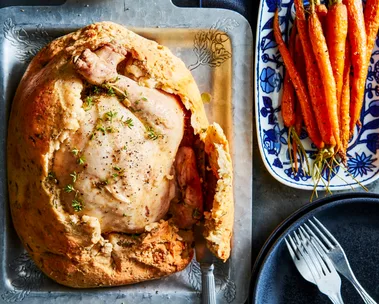 chicken in a salt crust with hole cut out of top with roasted carrots on the side