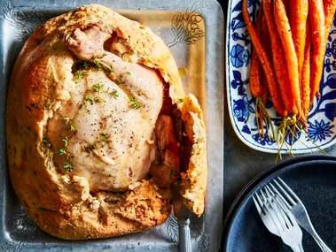 chicken in a salt crust with hole cut out of top with roasted carrots on the side