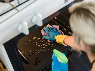 Person cleaning oven with spray and rubber gloves