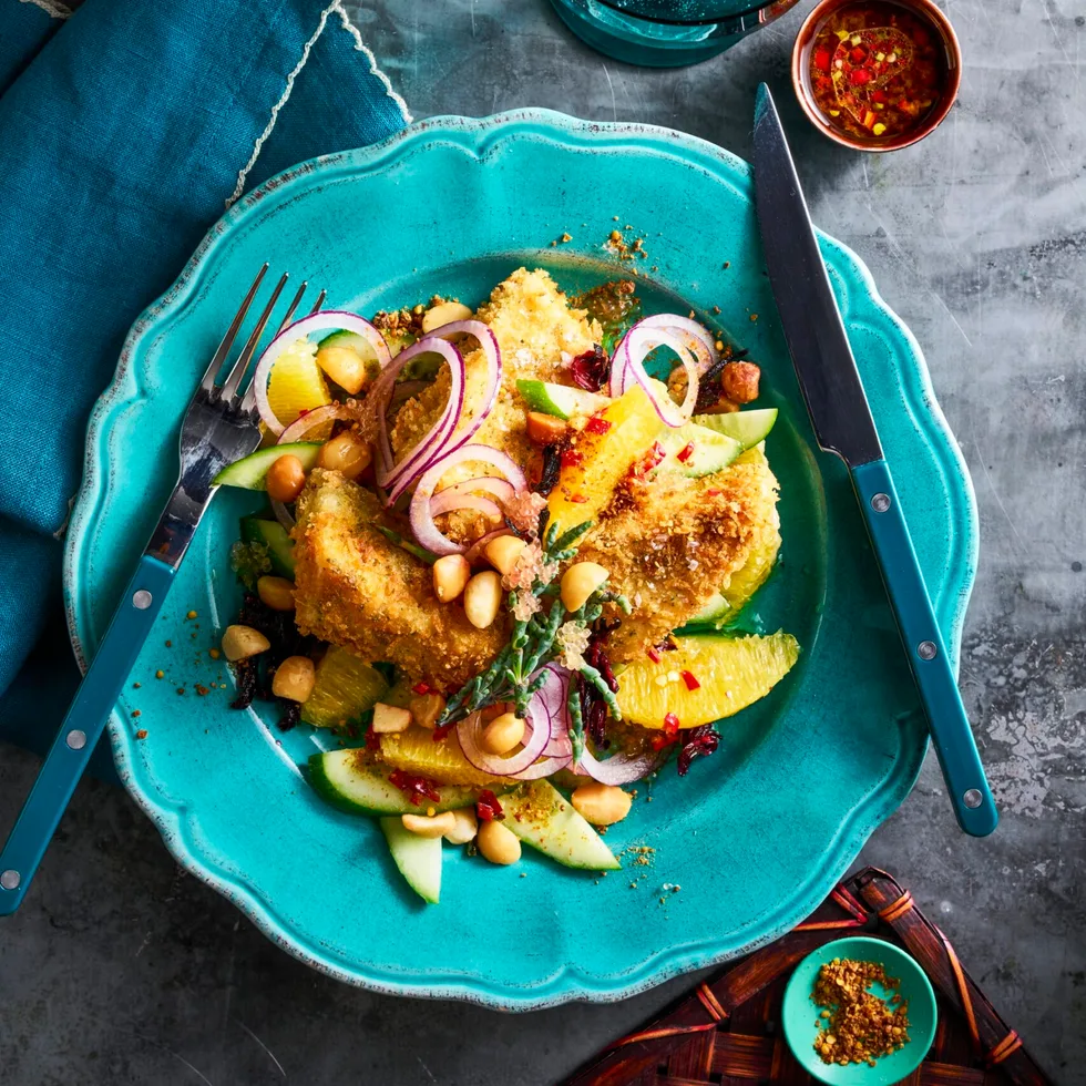 crumbed barramundi on blue plate with bush salad surrounding it