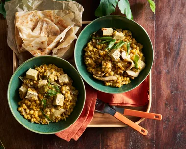 tofu and lentil vegetable stew in two green bowls with naan on the side