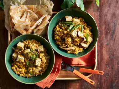 tofu and lentil vegetable stew in two green bowls with naan on the side