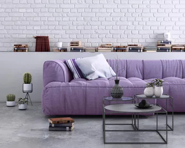 purple couch with cushions on it with white painted brick wall behind it