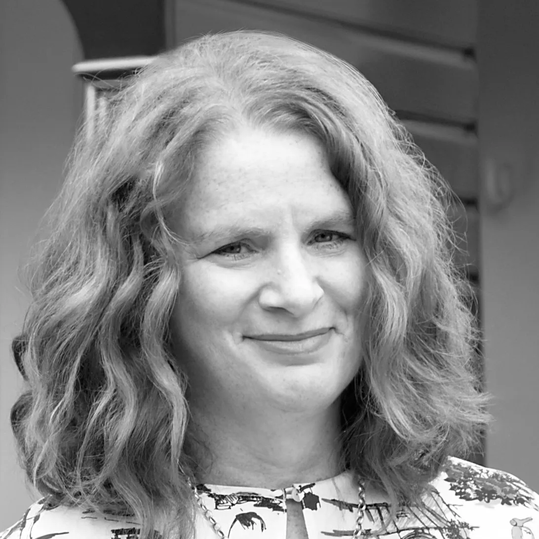 A woman with wavy hair smiles in a black and white portrait.