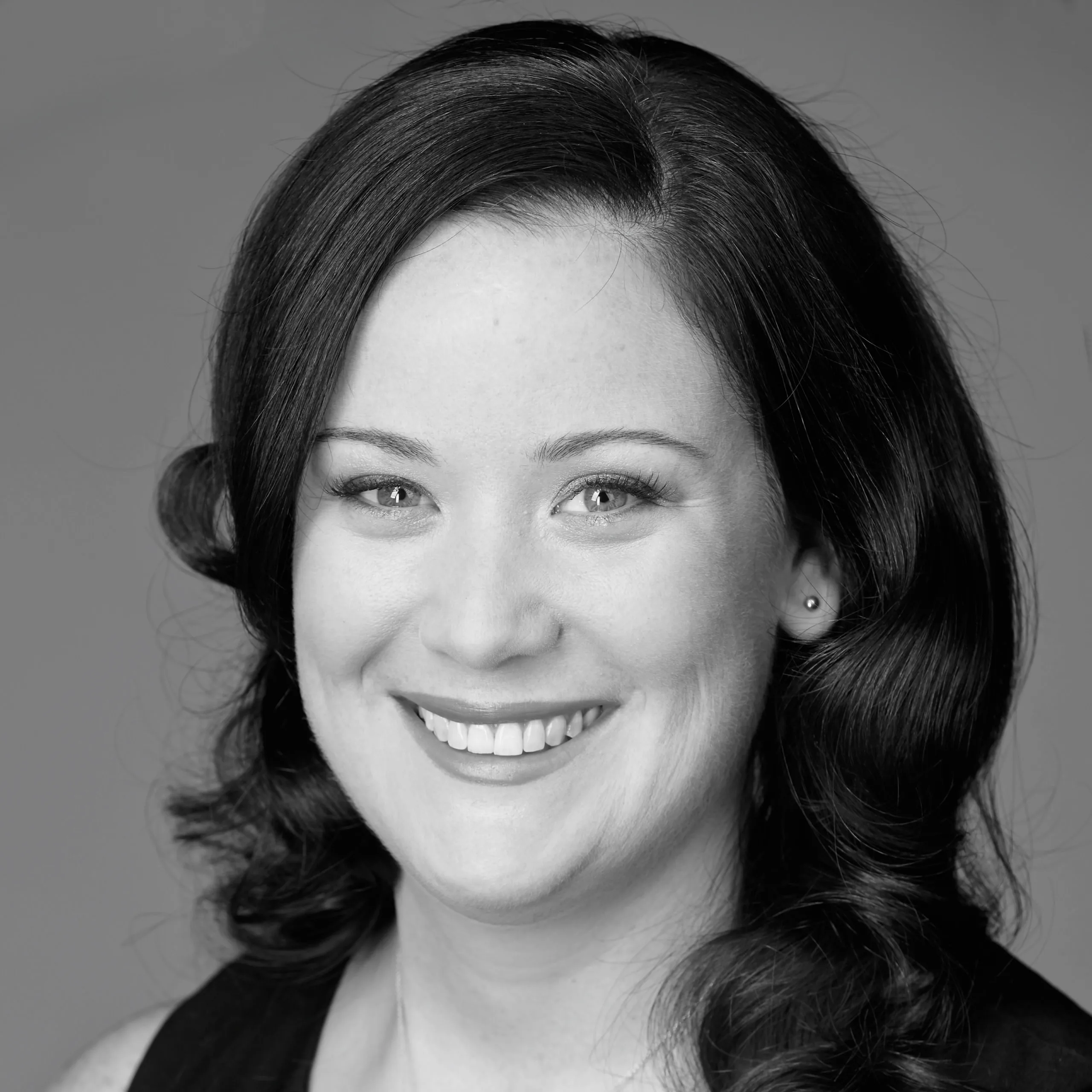 A woman with dark hair smiling in a black and white portrait.