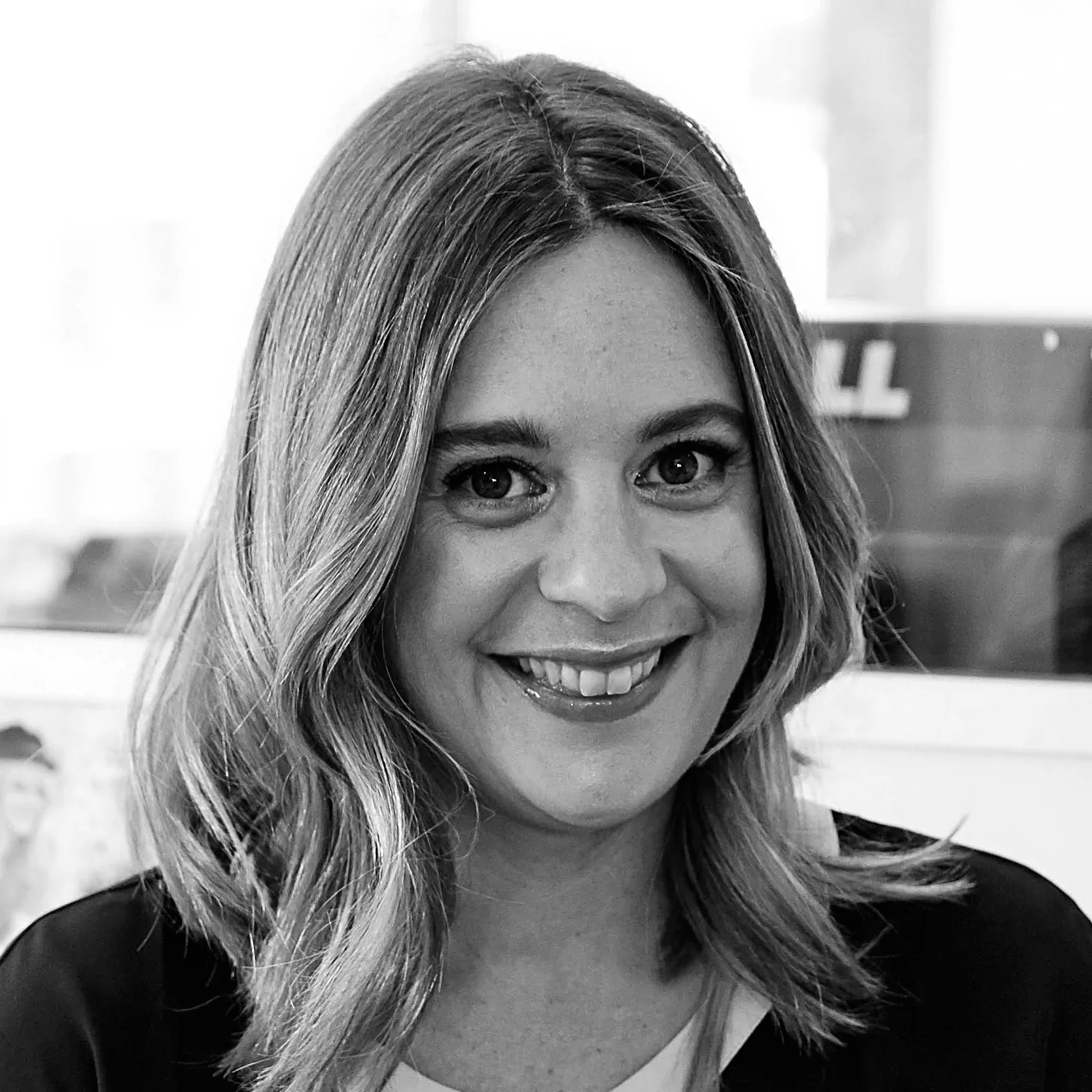 A woman with shoulder-length hair smiling in a black and white photograph, indoors.