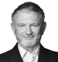 Black and white portrait of a smiling man with a beard, wearing a suit jacket and shirt.