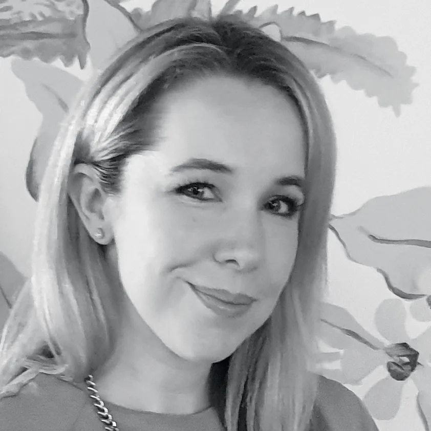 A woman with light hair smiling at the camera, with a floral background in grayscale.