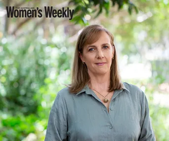 A woman in a light green shirt stands outdoors with blurred greenery behind her, featured in The Australian Women's Weekly.