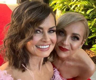 Two smiling women posing together on the red carpet, with greenery in the background.