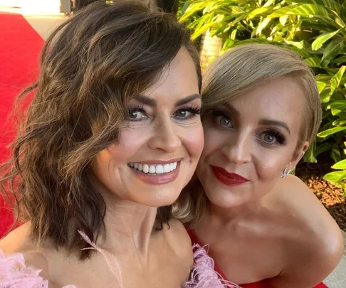 Two smiling women posing together on the red carpet, with greenery in the background.