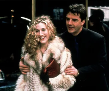 "Carrie Bradshaw and Mr. Big from 'Sex and the City' smiling together while walking, Carrie wearing a fur coat."