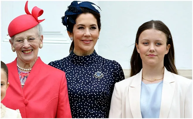 Three women standing together, two older women, one in red and one in navy, and a young girl in white, all smiling.