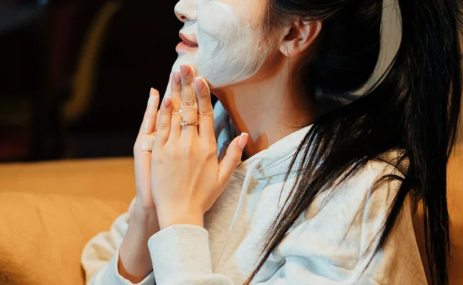 Woman in a hoodie with a face mask on, clasping her hands near her chin.