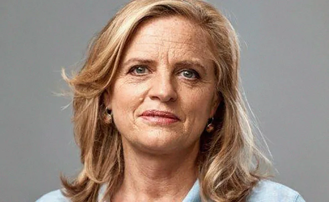 A woman with shoulder-length blonde hair and a light blue shirt, looking at the camera with a neutral expression.
