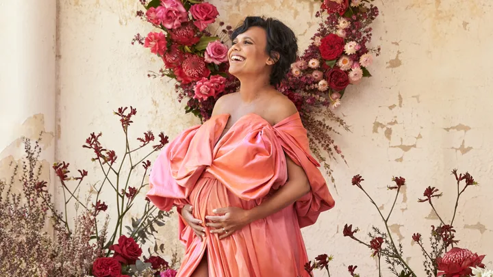 A woman in a vibrant pink dress poses joyfully in front of floral arrangements.