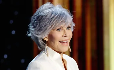 A smiling woman with short silver hair and dangling earrings wearing a white outfit.