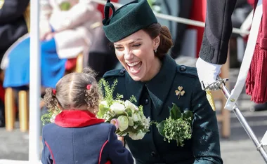 A woman in a dark green outfit smiles and receives flowers from a young girl with pigtails.