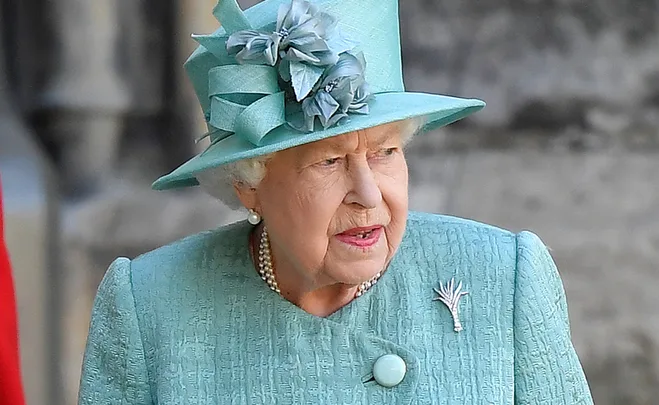 Elderly woman in a teal dress and hat with floral decoration, wearing pearls, looking to the side.