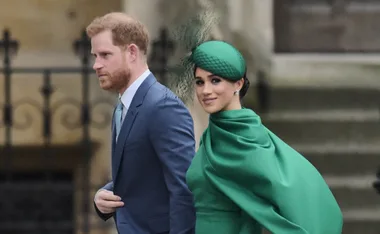 A man in a blue suit and a woman in a green outfit walk side by side outdoors.