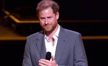 A man in a suit holding a microphone on stage, smiling slightly.