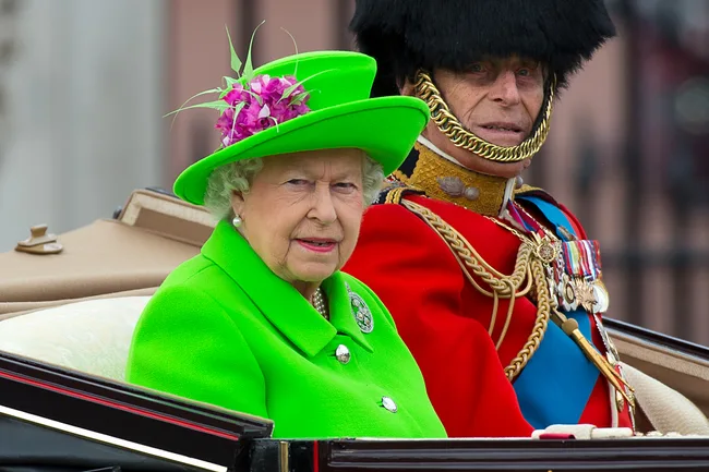 Royal procession: woman in bright green attire with a man in red military uniform.