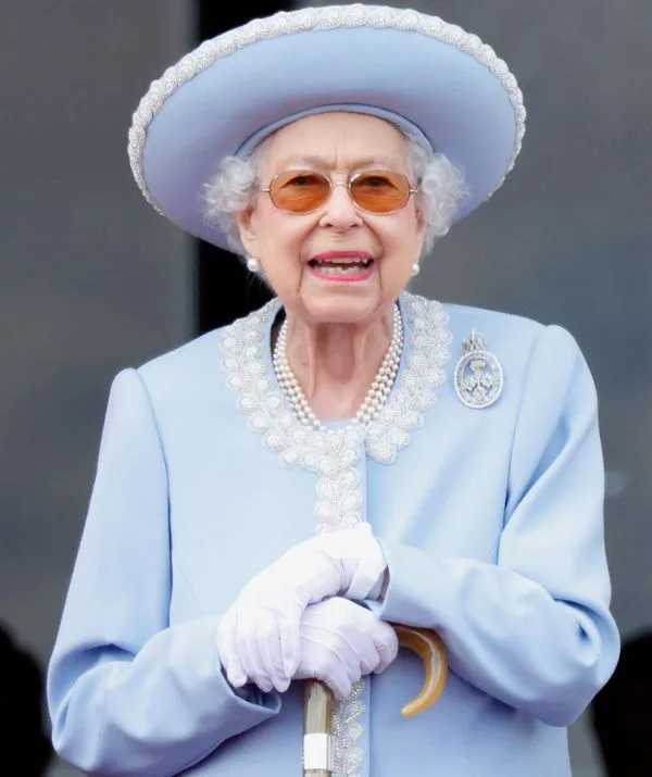 I don't know who this is, but the image shows an elderly woman in a light blue outfit, wearing gloves and holding a cane.