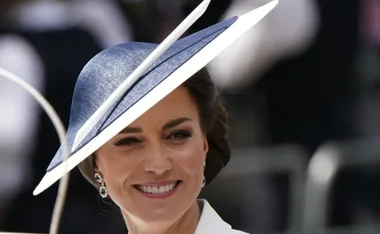 A woman smiling, wearing a large blue hat, with blurred background.
