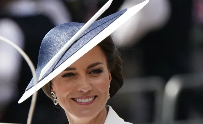 A woman smiling, wearing a large blue hat, with blurred background.