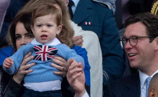 A child in a Union Jack sweater is held by a woman, with a man smiling nearby.