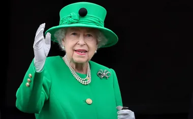 Queen Elizabeth II in a green outfit and hat, waving during the Platinum Jubilee celebration.